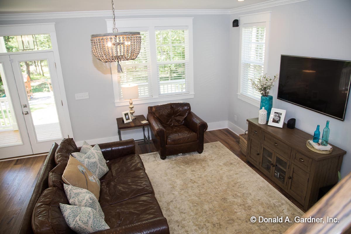 Interior view of a living room with leather sofa, armchair, entertainment console, and doors leading outside.
