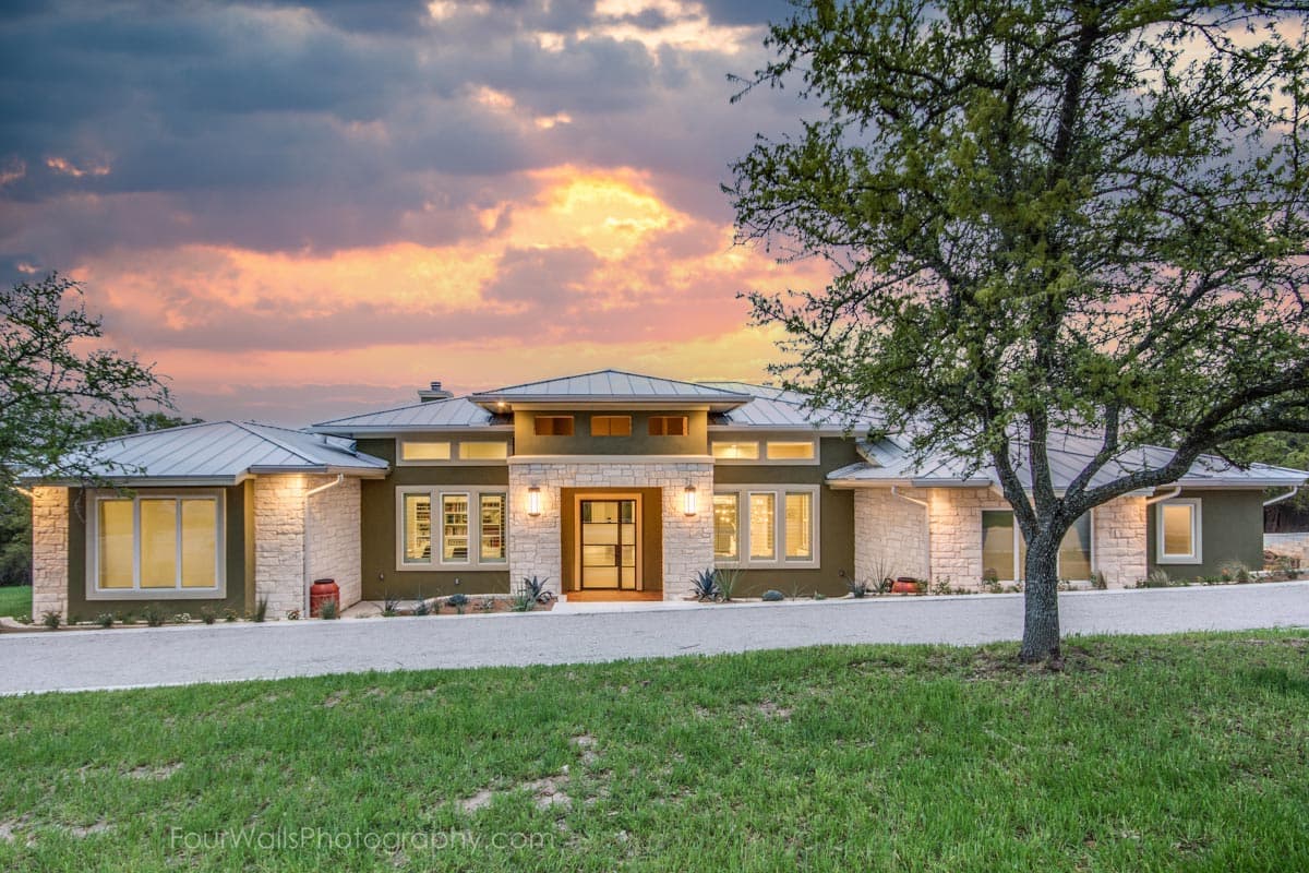 House plan exterior with modern design. Features include flat roof, stone facade accents, and a large entry door with sidelights. One-story home.