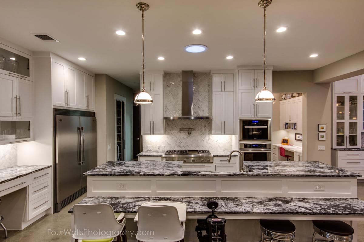 Contemporary kitchen with white cabinets, stainless steel appliances, marble countertops, and pendant lighting over an island.