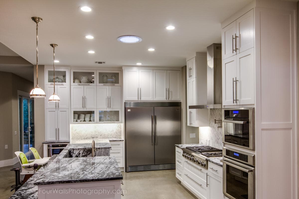 Kitchen with white cabinetry, dual ovens, stainless steel appliances, marble island, and pendant lighting.