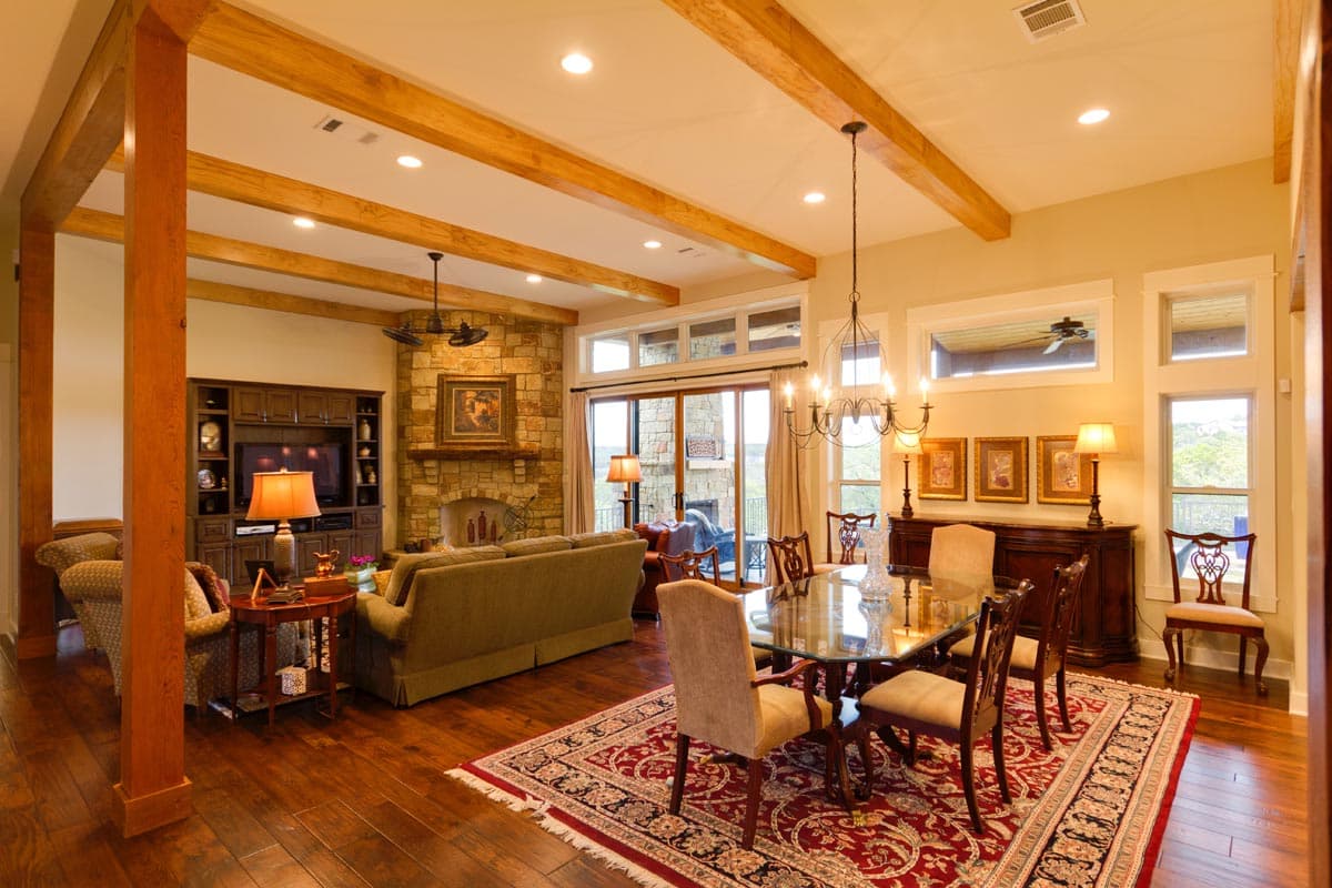 Interior view of a great room with a stone fireplace, dining table, and exposed wooden beams on the ceiling.