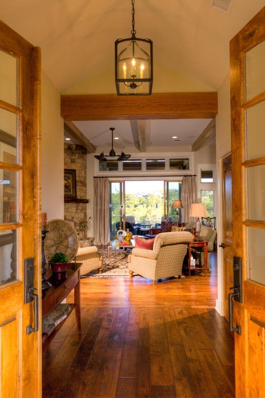 Interior view: Living room with stone fireplace, vaulted ceiling with exposed beams, and large sliding glass doors opening to a scenic view.