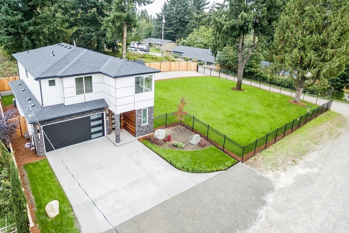 Modern two-story house exterior with a two-car garage, large windows, white siding, and stone accents.