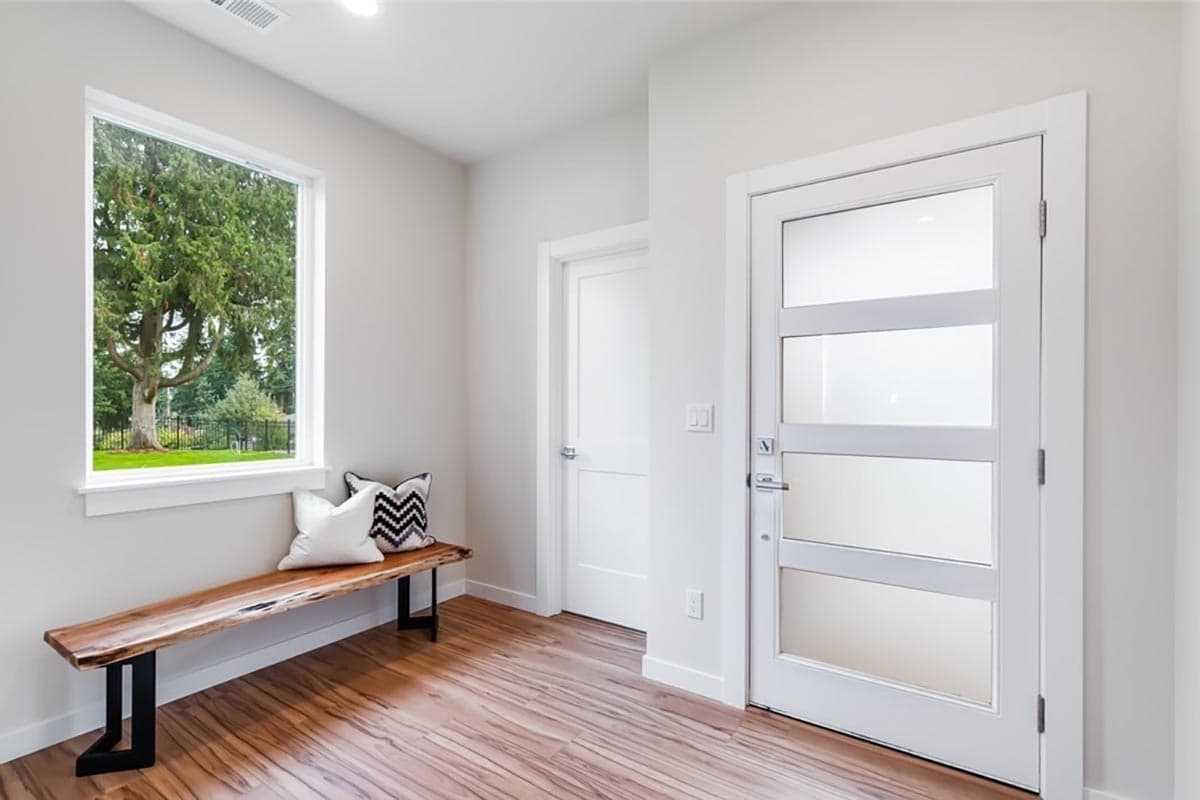 Interior view of a hallway with a live-edge bench, a large window, and a modern door with frosted glass panels.