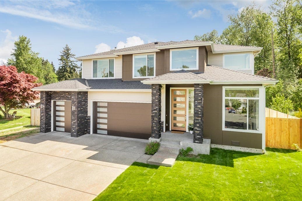 House plan exterior. Two-story modern style home with stone-clad columns, horizontal garage doors, and a combination of shed and gable rooflines.