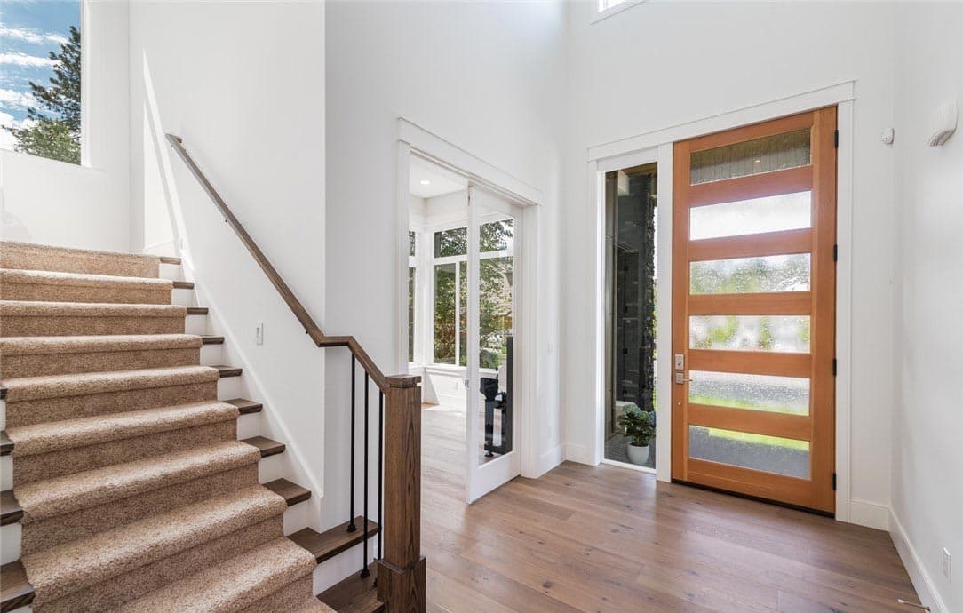 Interior entryway with carpeted staircase, wood floor, glass-paneled wood door, and glass door to sunroom.