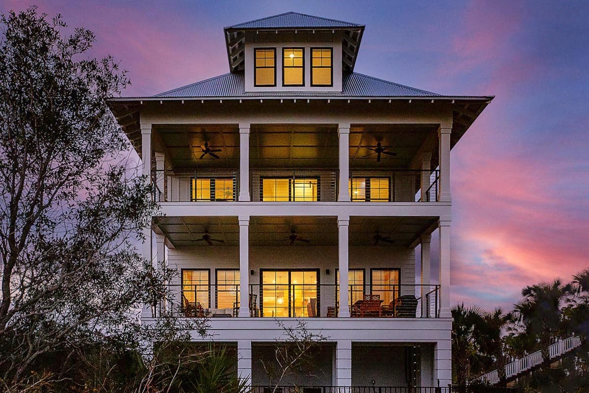 House plan exterior. Three-story coastal home with multiple balconies supported by columns. Features include a metal roof and a dormer.