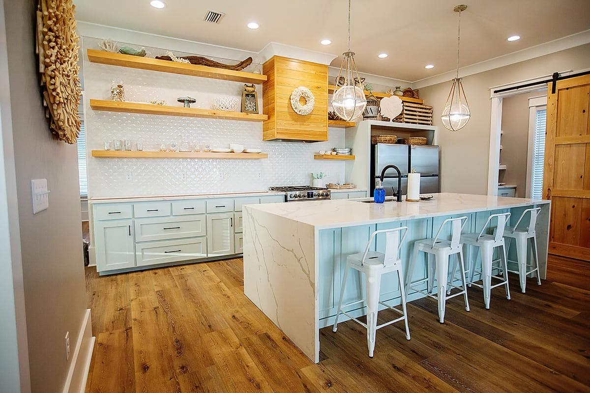 Kitchen featuring a large island with seating, light blue cabinetry, open shelving, and a wood-paneled range hood.