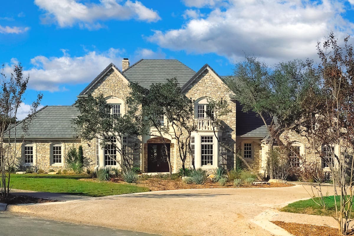 House plan exterior. Two-story home with stone facade, multiple gables, a balcony, and a slate roof.