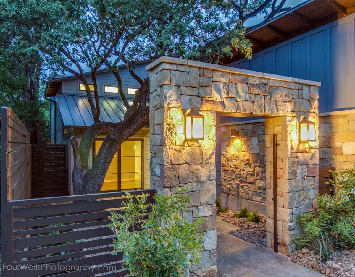 House plan exterior with stone archway, metal roof, and horizontal siding. Features integrated lighting.