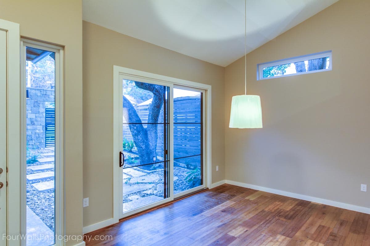 Interior view of a room with vaulted ceiling, sliding glass doors to yard, and a pendant light.