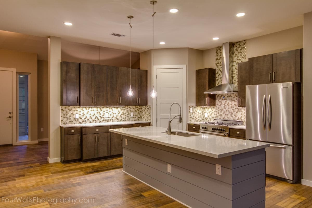 Kitchen interior with dark wood cabinets, a large island with sink, stainless steel appliances, and mosaic tile backsplash.