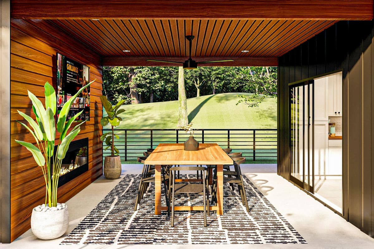 Covered patio with wood-paneled ceiling, fireplace, dining table, and adjacent interior kitchen area.