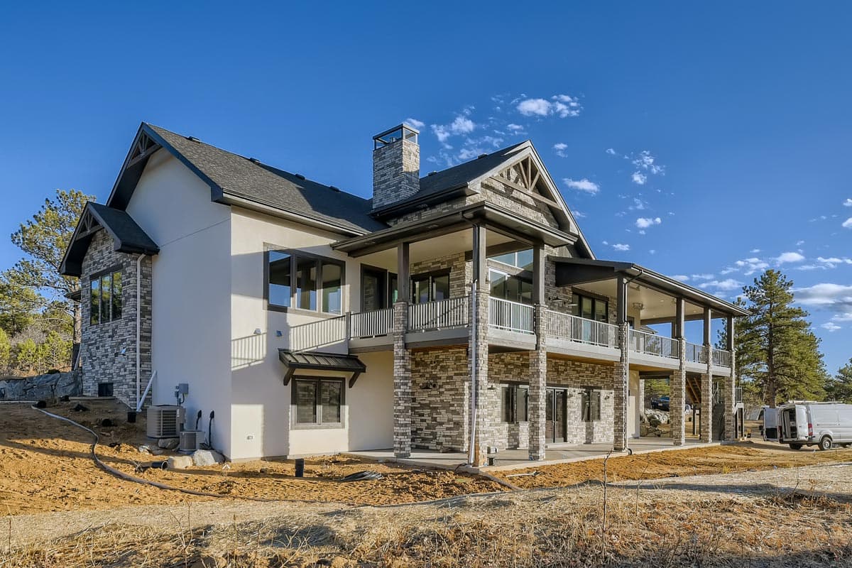 House plan exterior of a multi-story residence with stone and stucco facade, wide covered porches, gables, and a prominent stone chimney.