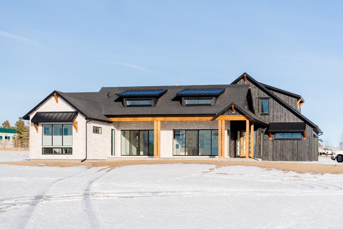 Modern house plan exterior with white stone, dark wood siding, covered entry, large windows, and two dormer windows.