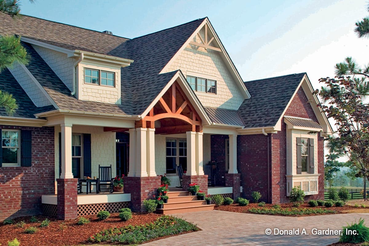House plan exterior: Two-story home with a covered porch, dormer, gables, and brick and shingle siding.