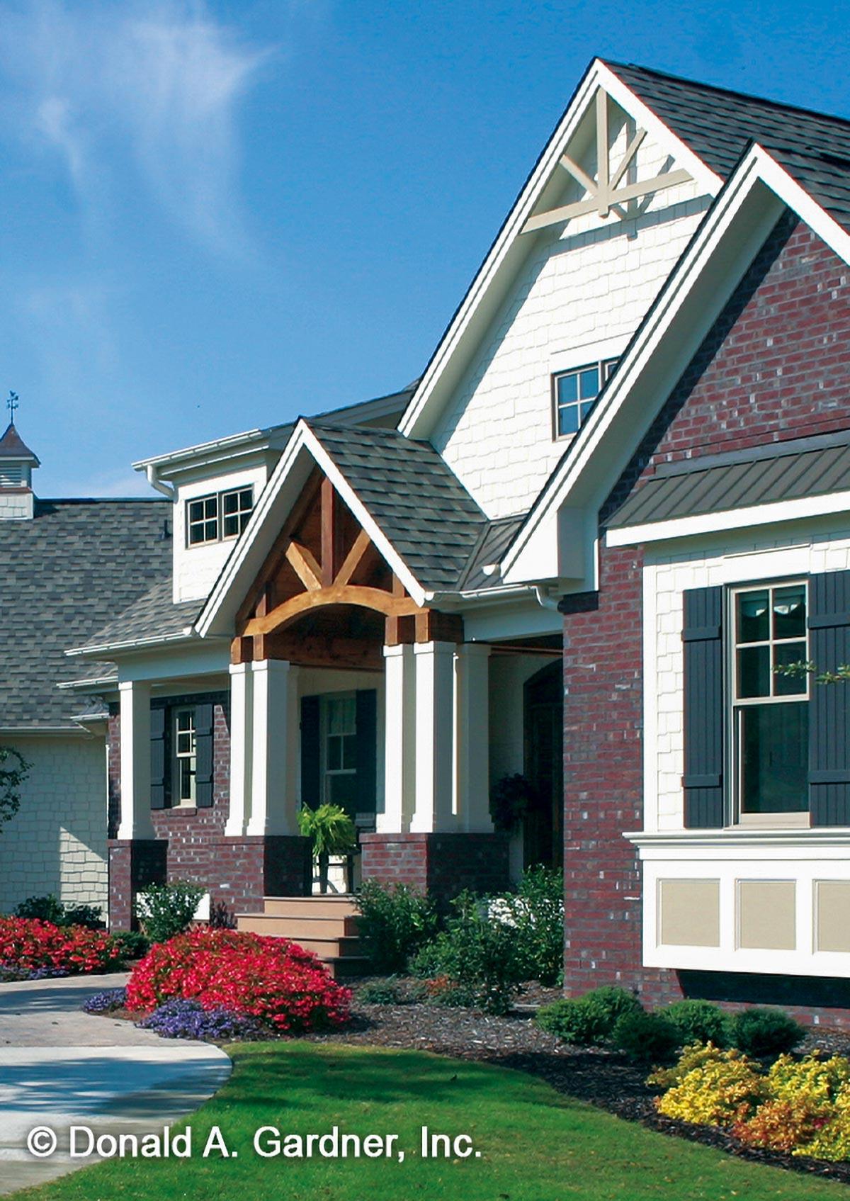 House plan exterior with a brick base, white siding, gables with decorative trusses, and a covered entry with timber framing.