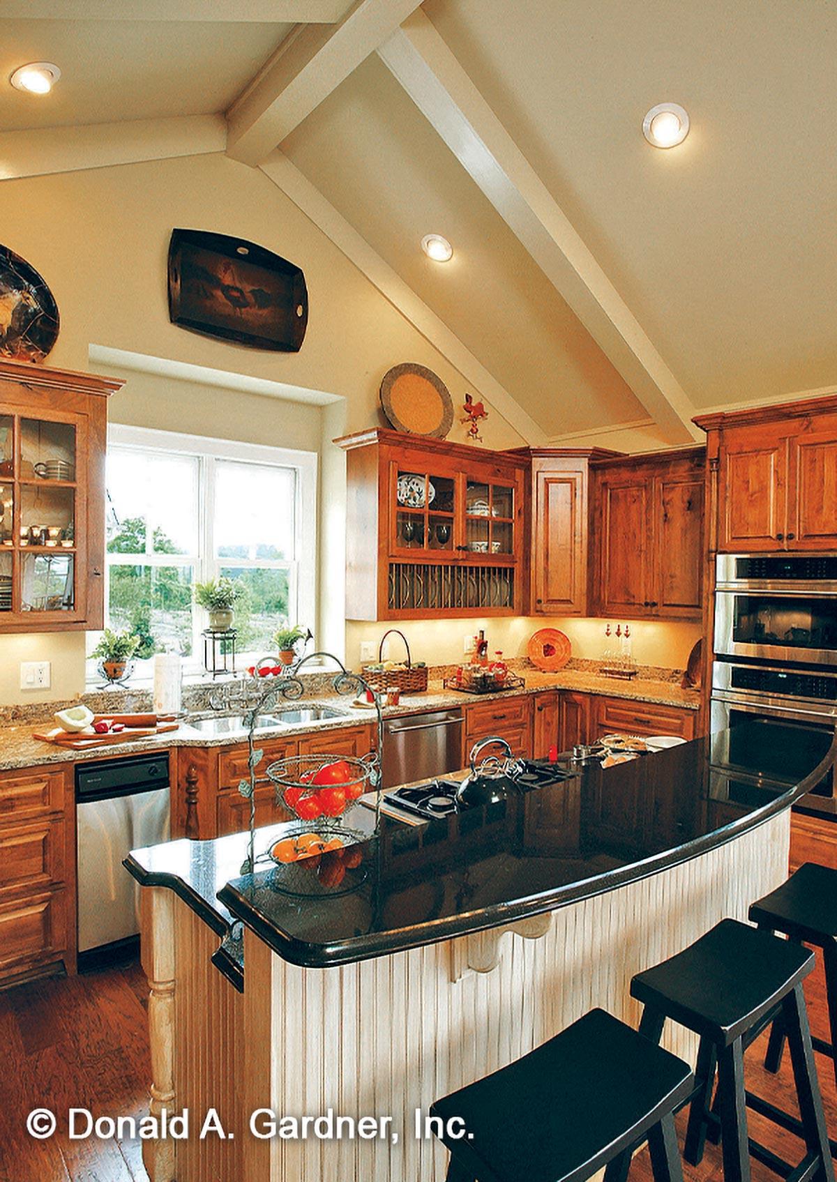 Kitchen interior with vaulted ceiling, exposed beams, granite countertops, island with cooktop, and wood cabinetry.
