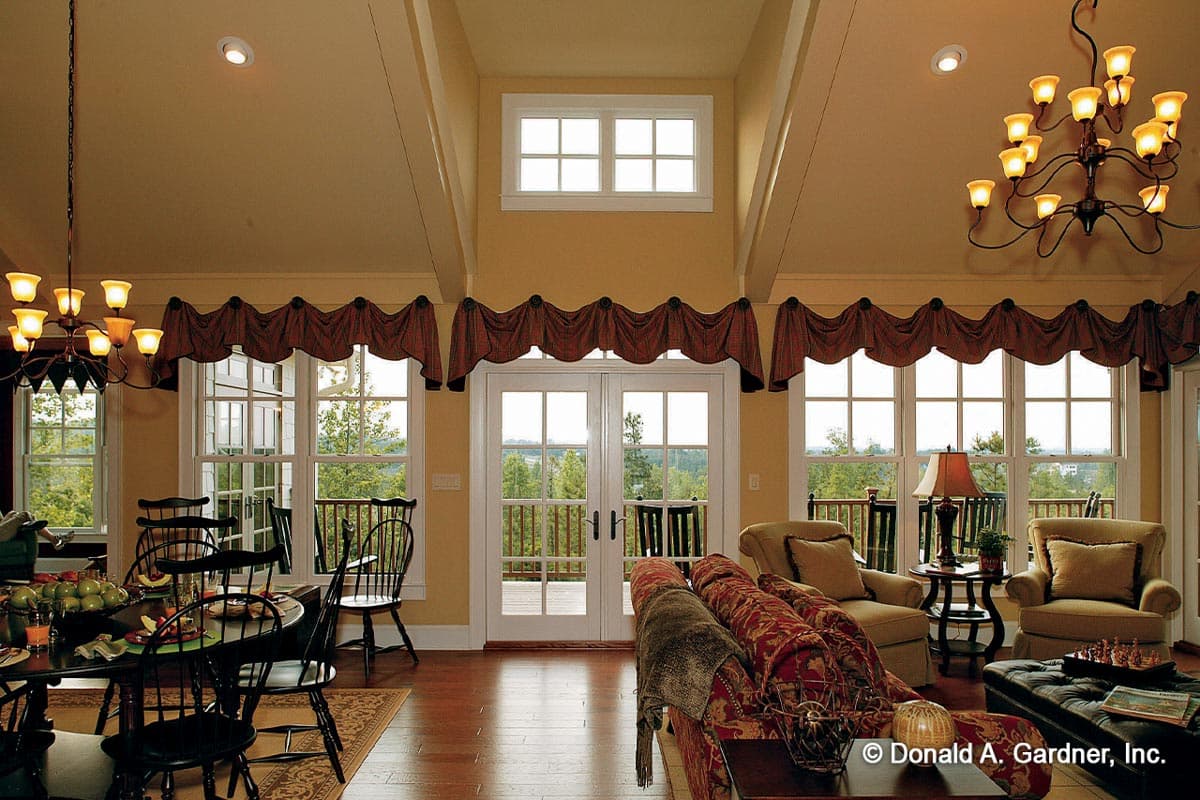Open-concept living and dining area with vaulted ceiling, large windows, double doors to balcony, and hardwood floors.