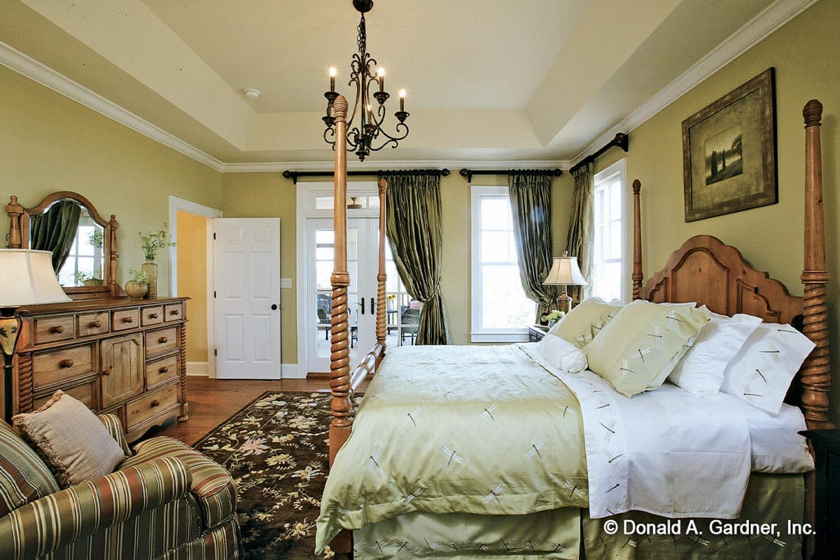 Bedroom with four-poster bed, tray ceiling, dresser, and double doors leading outside.