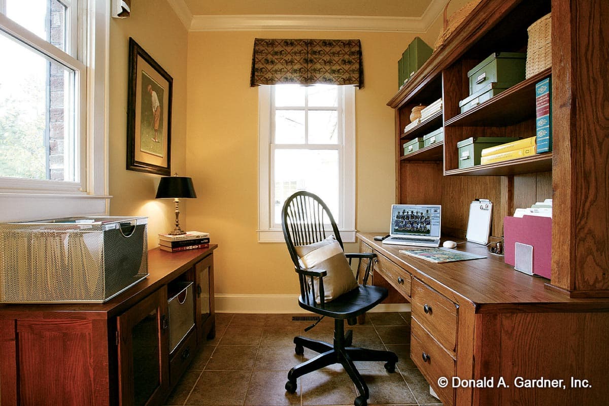 Office interior featuring a wooden desk with built-in shelving, chair, and a window.