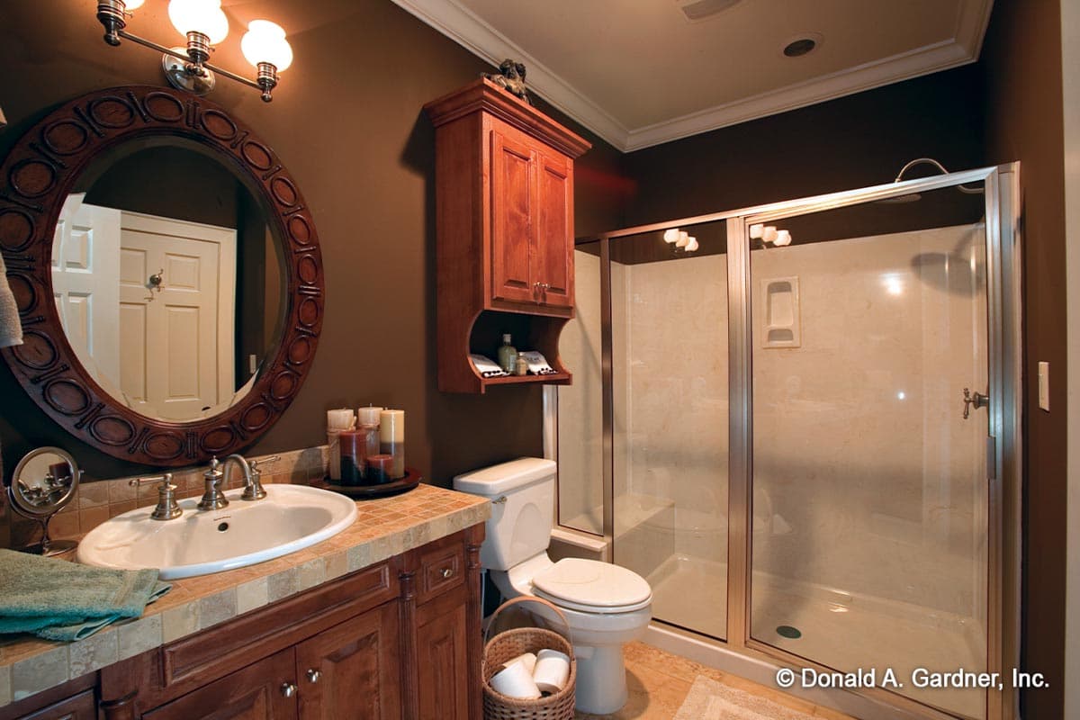Bathroom featuring a vanity with oval sink, wood cabinetry, decorative mirror, glass-enclosed shower, and toilet.