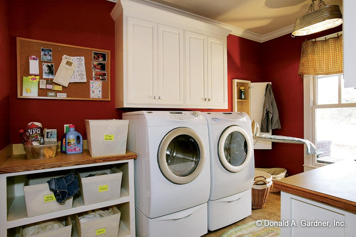 Laundry room with white front-loading washer and dryer, overhead cabinets, corkboard, and storage shelves.