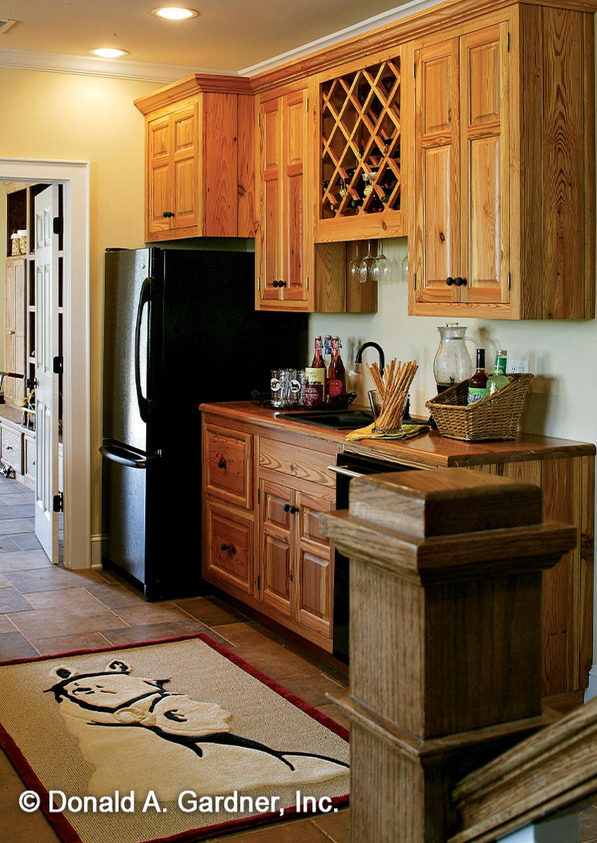 Kitchen wet bar with wooden cabinetry, wine rack, sink, and black refrigerator. Open doorway to another room.