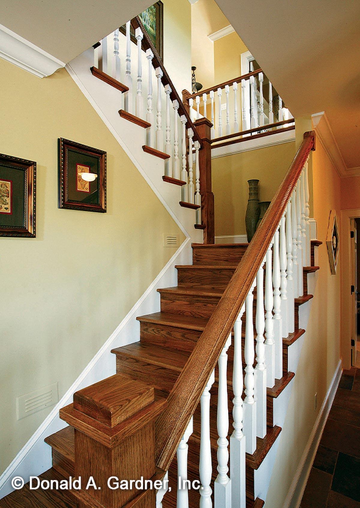 Interior view of a wooden staircase with white balusters and wood treads, leading to an upper landing.