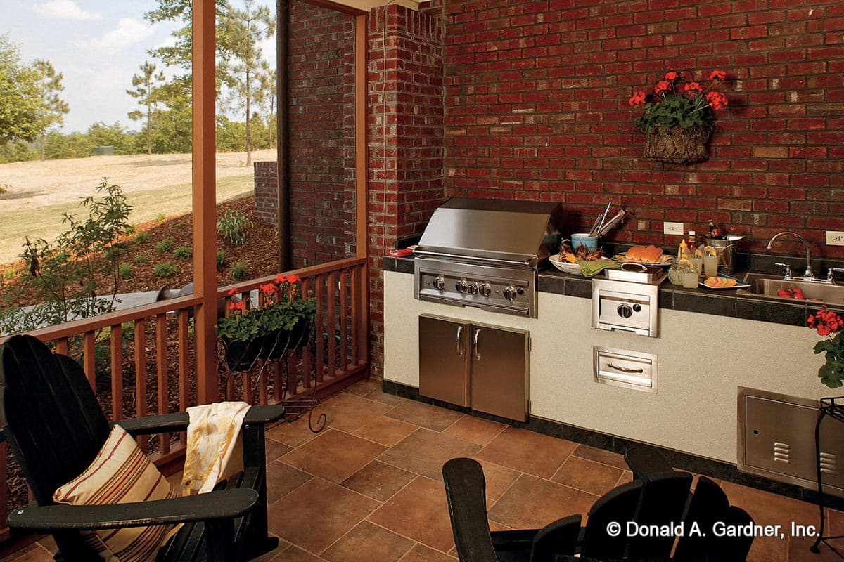 Outdoor kitchen with stainless steel grill, sink, and storage cabinets against brick wall.