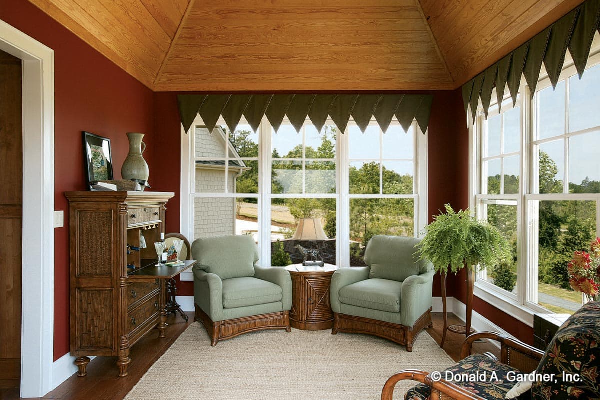 Sunroom with wood plank ceiling, large windows, two upholstered chairs, and a decorative cabinet.