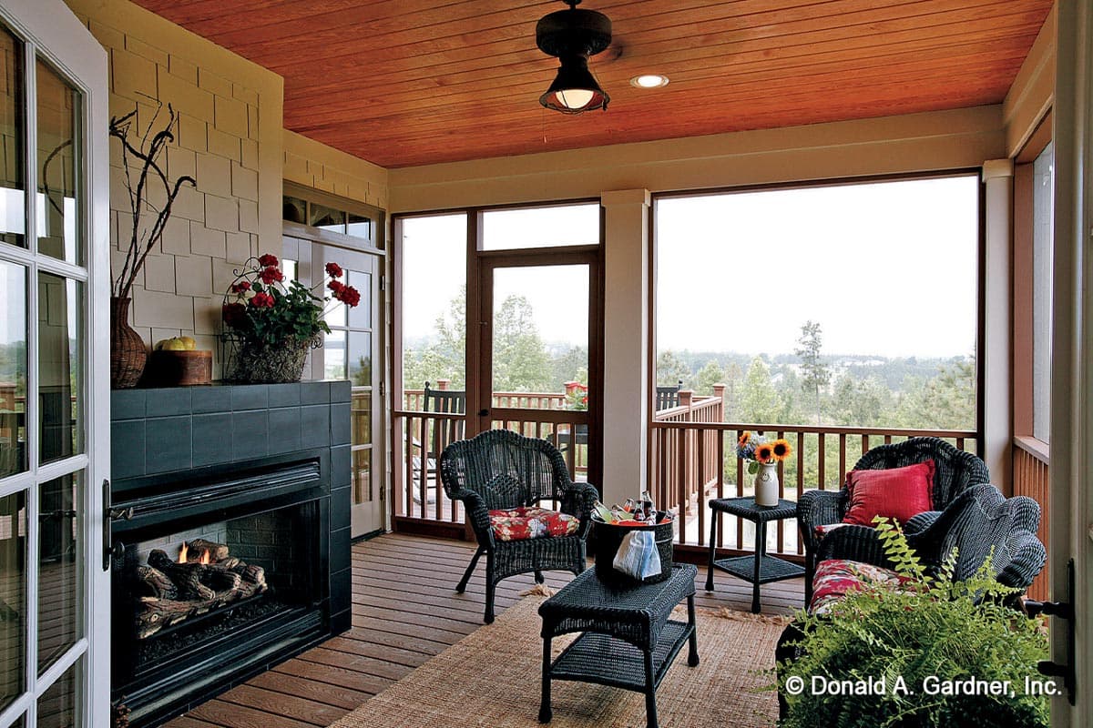 Covered porch with wood ceiling, fireplace, wicker furniture, and deck overlooking trees.