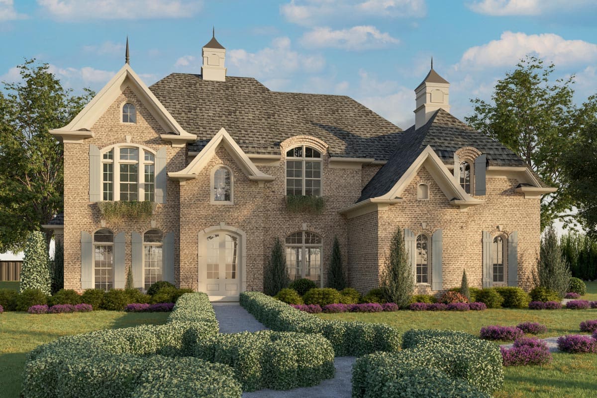 House plan exterior featuring a two-story brick facade. Notable features: gables, dormers, and a slate roof. Landscaping includes hedges and gardens.