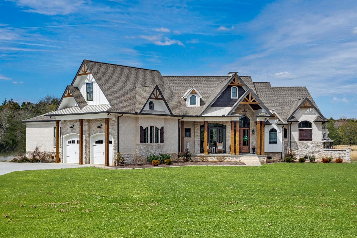 House plan exterior. Two-story Modern Farmhouse with gables, arched windows, and a covered front porch with timber-framed columns.