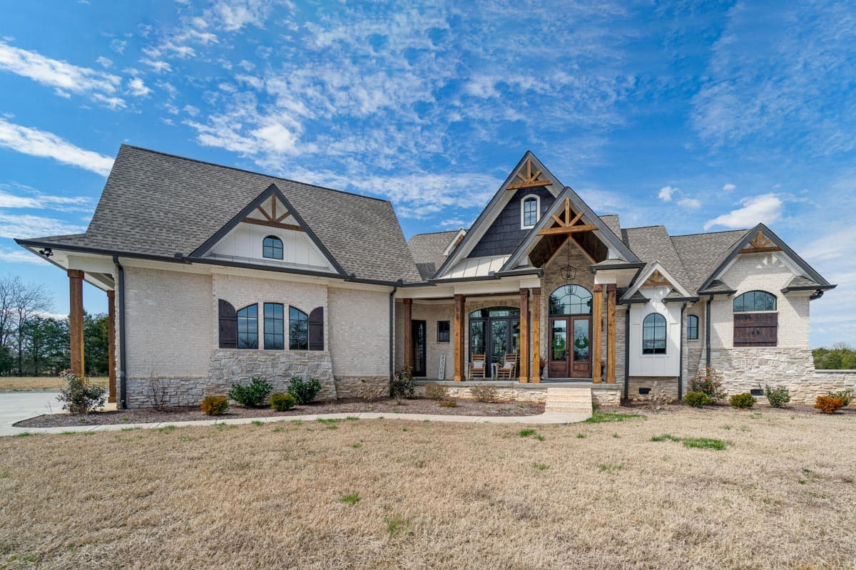 House plan exterior: Modern Farmhouse style, two stories, featuring a covered porch, multiple gables with exposed wood beams, and stone accents.