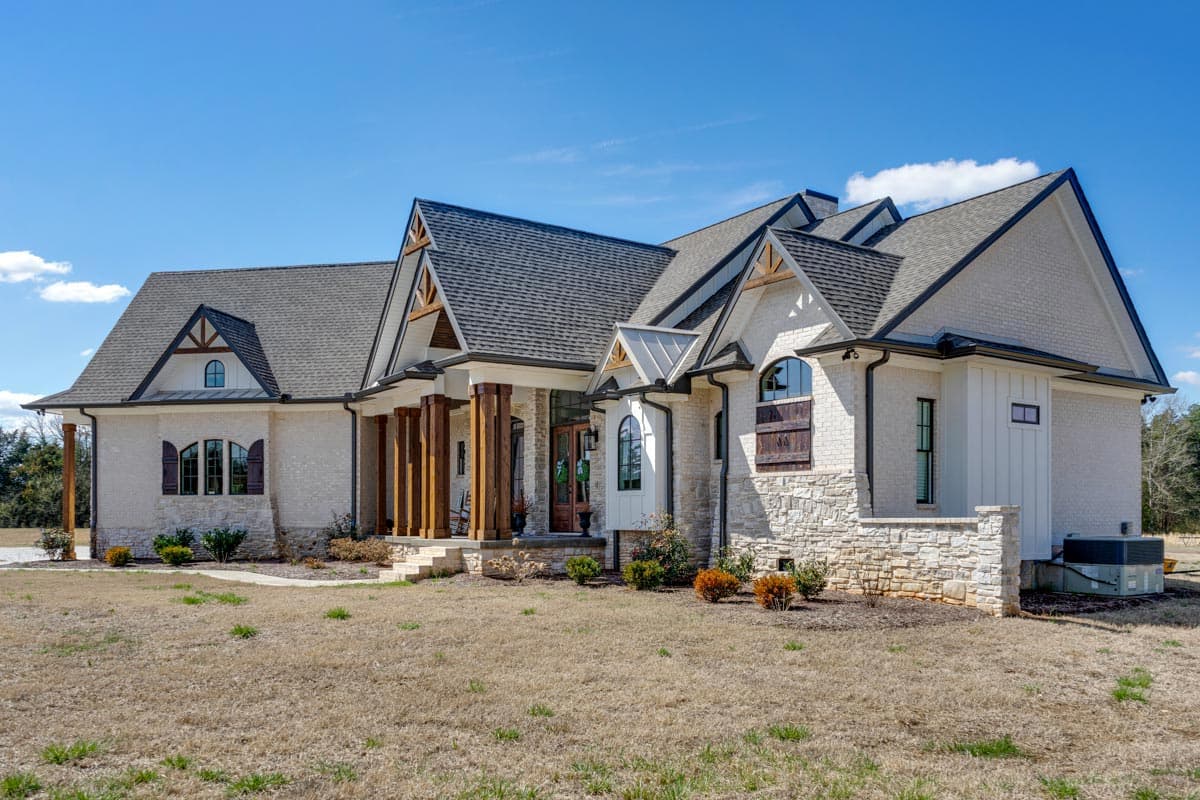 House plan exterior: Modern Farmhouse style, multiple gables with exposed beams, prominent columned entry porch, stone and brick facade.