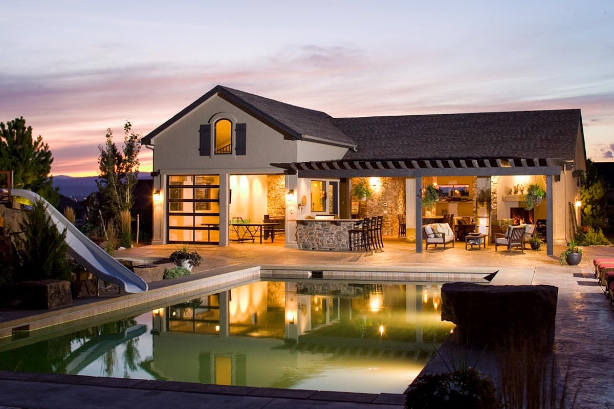 House plan exterior. Two-story home with pergola, stone facade, and glass garage doors. Features a swimming pool, outdoor fireplace, and bar.