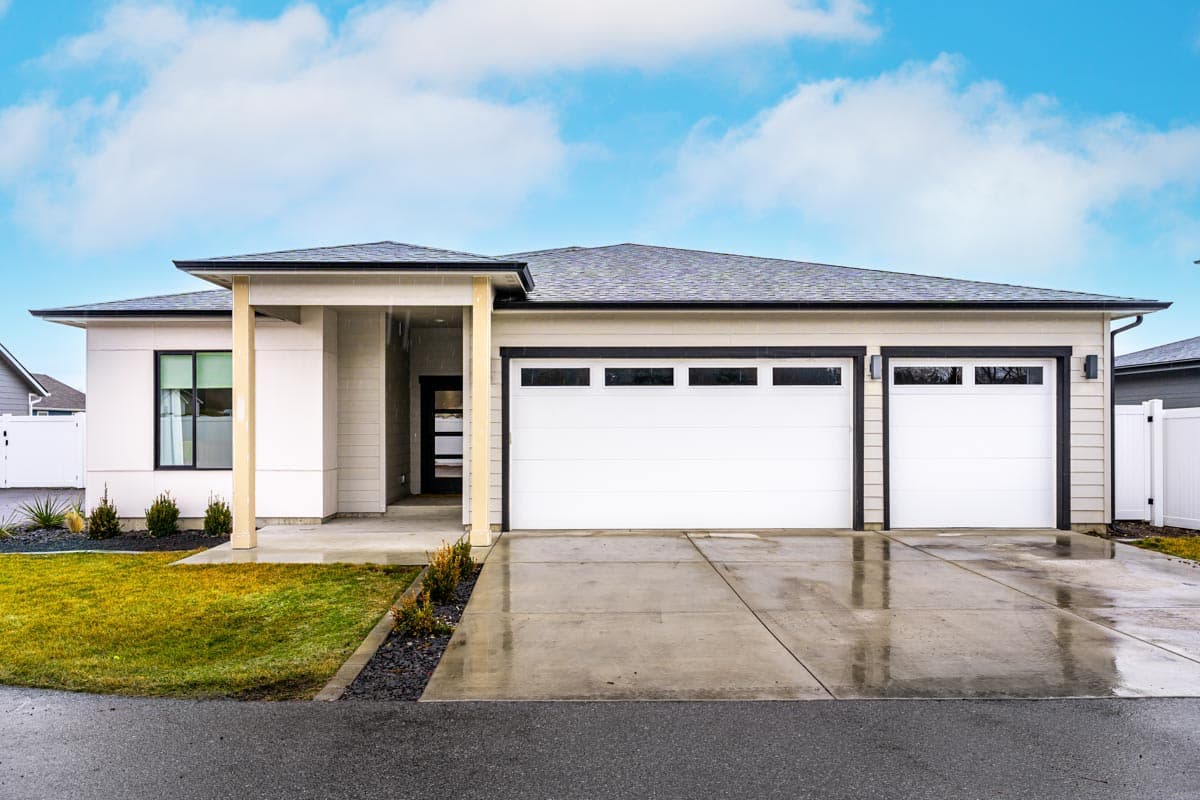 House plan exterior. Modern style, single story home with a covered entry, two-car garage, and a low-pitched roof.