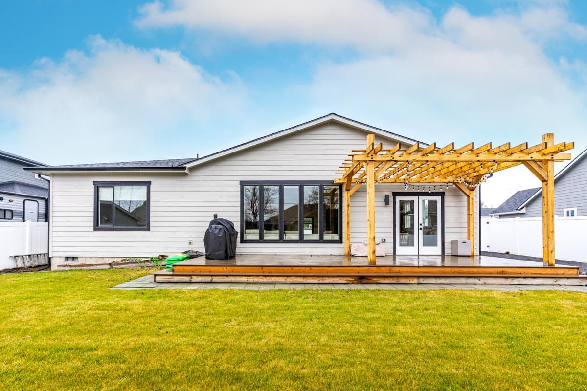 House plan exterior: One-story home with horizontal siding, a large multi-pane window, and a wooden pergola over double doors.