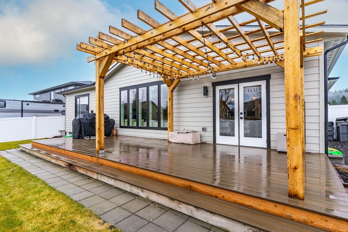 Modern house plan exterior with a wood pergola over a deck, double glass doors, and wide windows.