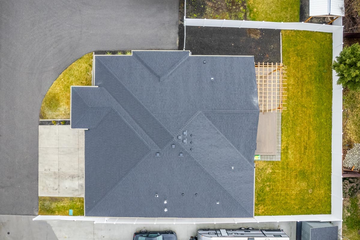 Aerial view of house plan exterior showing complex rooflines, driveway, and backyard deck with pergola.