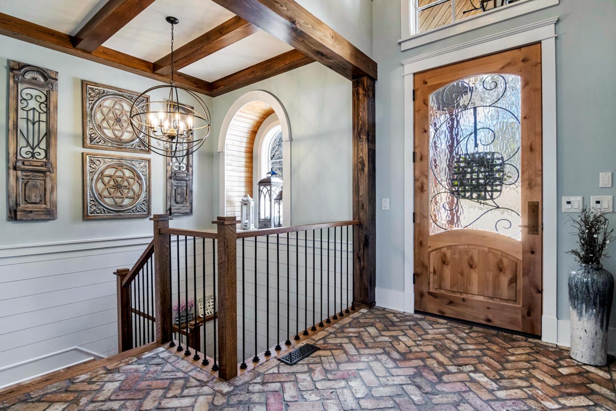 Entryway with wood door, metal-inset glass, beamed ceiling, decorative wall panels, and wood staircase with black balusters.