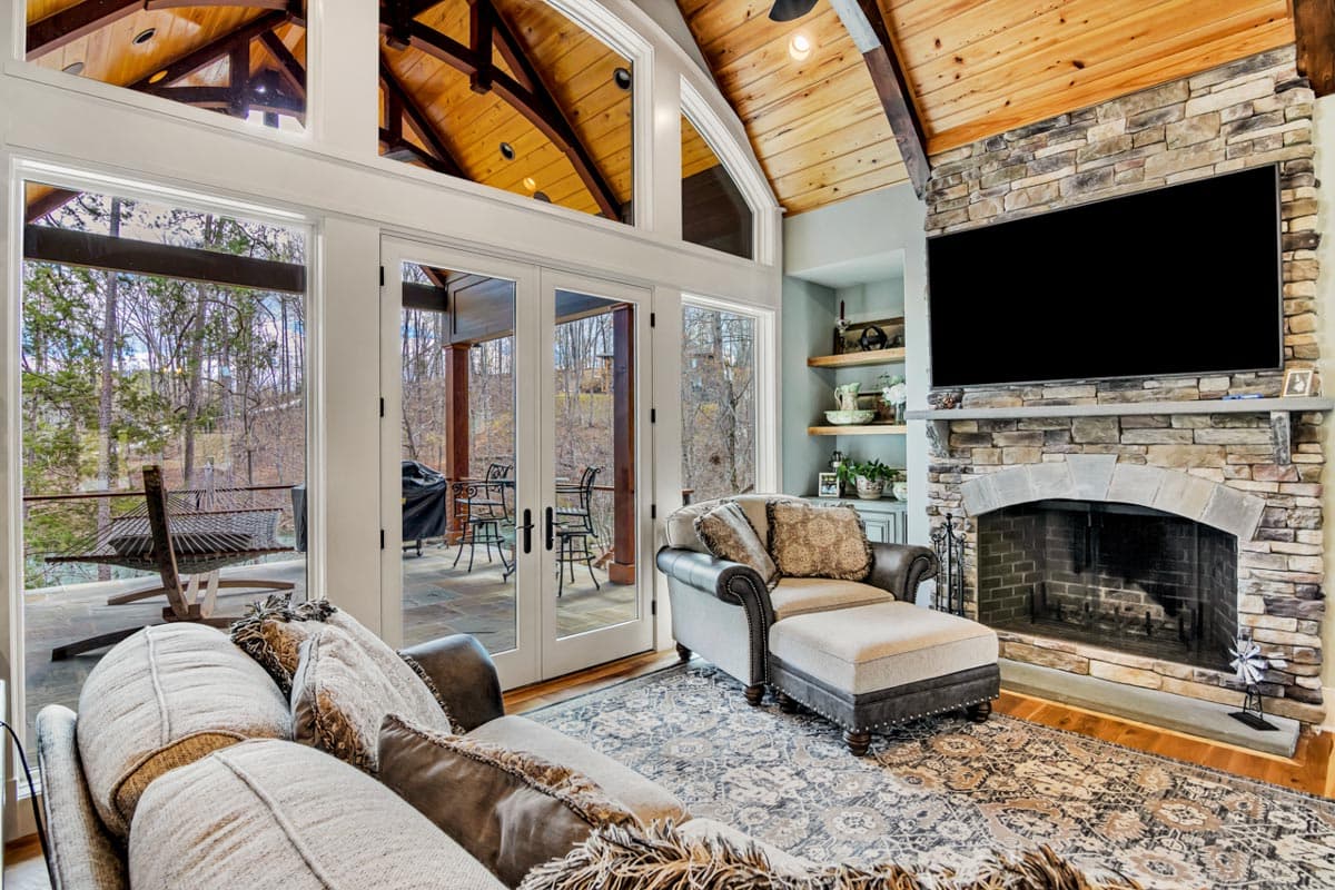 Great room with vaulted wood ceiling, stone fireplace, and French doors opening to a covered porch.