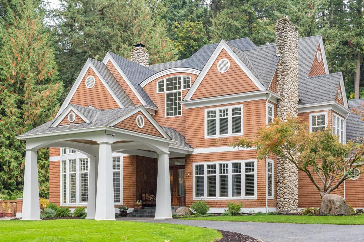 House plan exterior featuring a prominent stone chimney, arched dormers, and a covered porte-cochere with white columns.