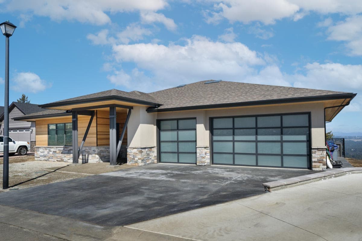 House plan exterior: Modern ranch style with a low-pitched roof, wood siding, stone accents, and two frosted glass garage doors.