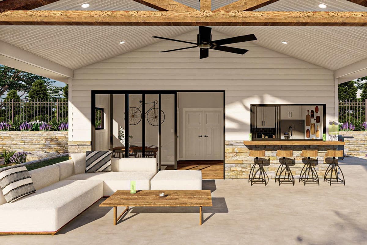 Covered outdoor living space with sectional seating, coffee table, and outdoor bar with stools and pass-through window.