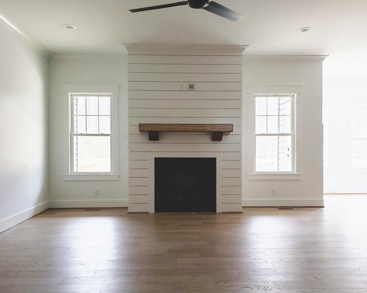 Great room with shiplap fireplace, wood mantel, two windows, and ceiling fan. Hardwood floors.