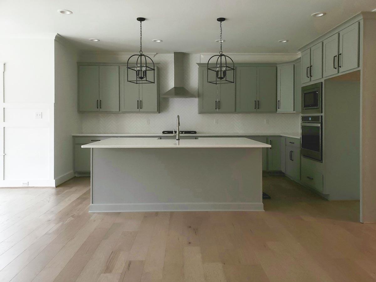 Kitchen interior with gray cabinets, large island with sink, stainless steel appliances, and pendant lighting.