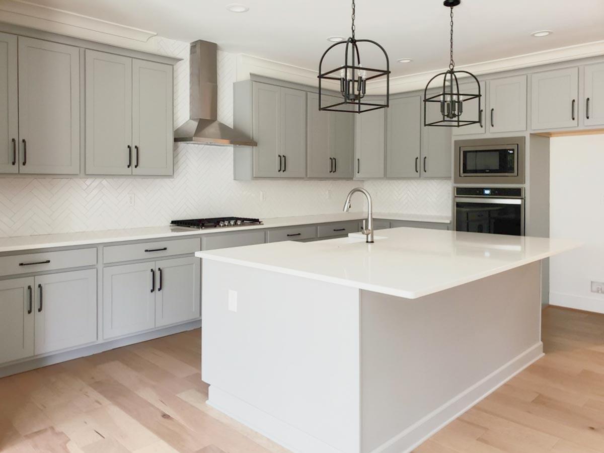 Kitchen with gray cabinetry, white quartz island, stainless steel range hood, gas range, and pendant lights.