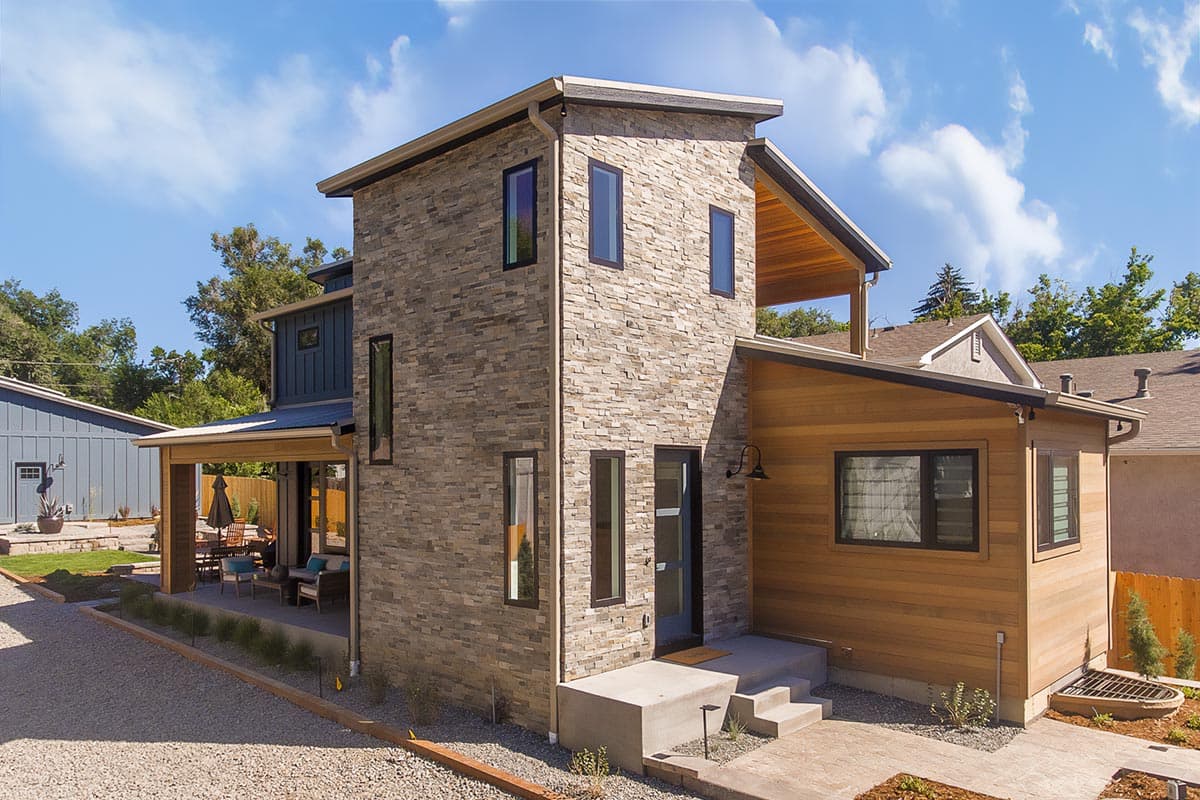 House plan exterior. Two-story modern house with stone facade, covered porch, and shed roof. Features include an outdoor living space.